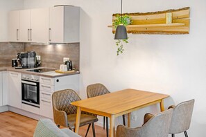 Une cuisine moderne avec des meubles blancs, une table à manger en bois et un luminaire suspendu.
