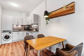 Une cuisine compacte dotée d’appareils électroménagers modernes, un coin repas avec une table en bois et des chaises en cuir, et un luminaire suspendu.