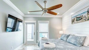 A bedroom with a bed, a ceiling fan, a painting, and a window.