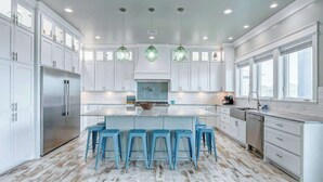 A modern kitchen with white cabinetry, a central island with stools, and pendant lighting.
