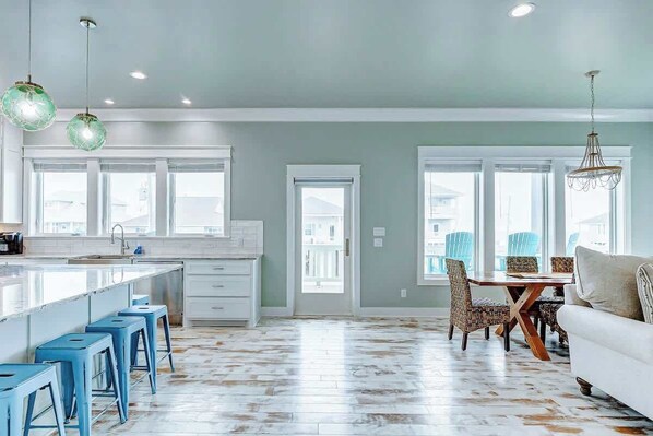 A modern kitchen with a large island, blue bar stools, and a dining area with patterned chairs and a white sofa. - Moon Pye, Pool, Dog Friendly (Crystal Beach)