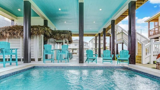 A swimming pool with turquoise chairs and a thatched roof structure.