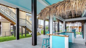 A pool area with a thatched roof, a bar, and outdoor seating.