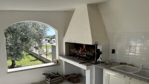 A kitchen with a built-in grill, a window overlooking a garden, and a tiled backsplash.