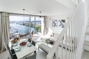 A modern living room with a dining area, large windows with a marina view, and a staircase. - 243-Fully Renovated-Puerto Banus Marbella Front Line Penthouse (Marbella)