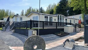 A mobile home with a black fence, a stone structure labeled 'Spruce Bank', and a gravel driveway. - The Shak, Tarbolton, Middlemuir Holiday Park (Tarbolton  Mauchline)