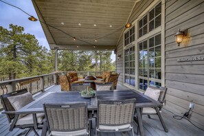 A covered outdoor seating area with a table and chairs, a sign reading "It's Five O'Clock Son," and a view of trees in the background.