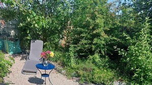 Une terrasse de jardin avec une table et des chaises, entourée de verdure et agrémentée d’un petit élément décoratif aquatique.