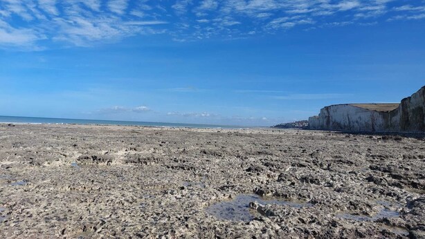 Une plage avec un terrain rocheux et des falaises en arrière-plan.
