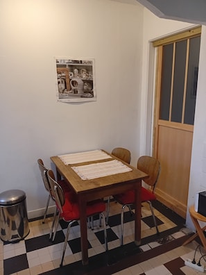 Ein Essbereich mit Holztisch, vier Stühlen, einem karierten Boden, einem Mülleimer und einem gerahmten Bild an der Wand.