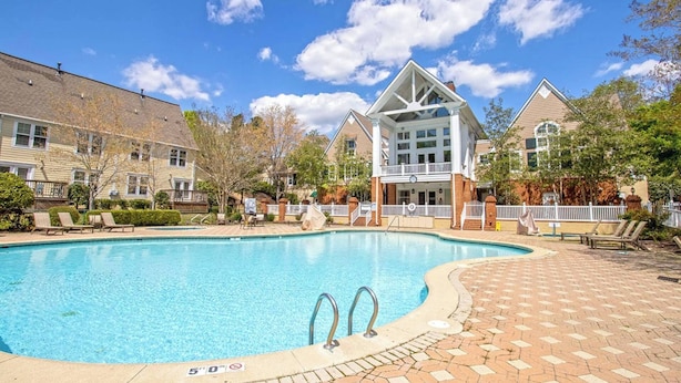 A swimming pool with a deck, surrounded by buildings with a mix of architectural styles, including a prominent white building with a balcony. - Spacious 3BR Cottage - Family Friendly Resort - Close to Theme Parks (Williamsburg)