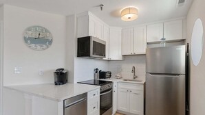 A modern kitchen with white cabinetry, stainless steel appliances, a microwave, oven, and a refrigerator. - 2BR Condo with Modern Amenities Steps to Beach! (Wildwood)