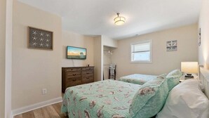 A bedroom with two beds, a dresser, a painting, and a window. - 2BR Condo with Modern Amenities Steps to Beach! (Wildwood)