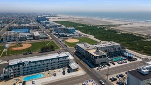 An aerial view of a hotel with multiple buildings, a parking lot, and a beach in the background. - 2BR Condo with Modern Amenities Steps to Beach! (Wildwood)
