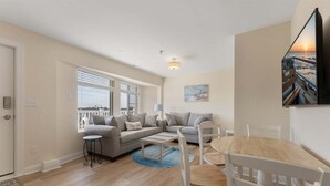 A living room with a sofa set, a dining table with chairs, a blue rug, and a painting on the wall. - 2BR Condo with Modern Amenities Steps to Beach! (Wildwood)