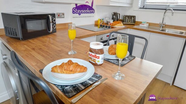 A compact kitchenette with a microwave, a toaster, and a sink. There is a breakfast setup with a croissant, Nutella, and orange juice.