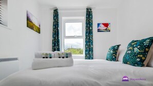 A hotel room with a bed, a window with curtains, and two wall-mounted paintings.