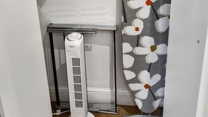 A compact room with a white radiator, a small table with a white cloth, and a wall-mounted ironing board with a floral pattern.