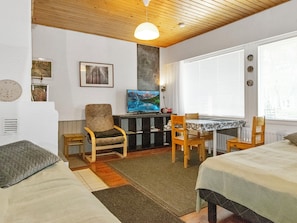 Una habitación con cama, una silla, una mesa, televisor y ventana con persianas.