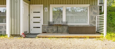 Un edificio con un porche cubierto, una puerta y una pequeña zona de estar al aire libre con dos sillas y una mesa.
