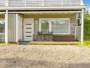 A building with a covered porch, a door, and a small outdoor seating area with two chairs and a table.