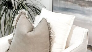 Un canapé blanc avec un coussin beige et un autre coussin blanc orné de franges.