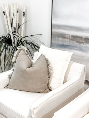 A white sofa with a beige pillow and a white cushion with fringe details.