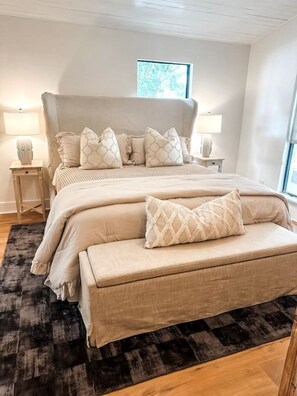 A bedroom with a large bed, two bedside tables, a bench, and a window.