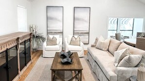 Un salon spacieux avec une table basse en bois, des canapés blancs et une grande fenêtre laissant entrer la lumière naturelle.