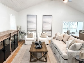 A spacious living room with a wooden coffee table, white sofas, and a large window providing natural light.