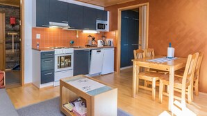Et kompakt køkken med moderne hårde hvidevarer, et spiseområde med træmøbler og en hyggelig indretning med trælofter.