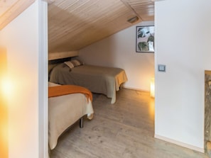 A bedroom with two beds, wooden flooring, and a sloped ceiling.