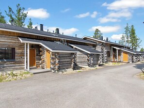 A row of log cabin-style buildings with wooden doors and a paved driveway.