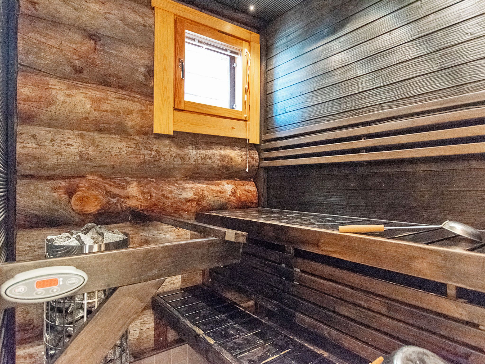 A log cabin interior with a wood stove, a window, and a metal sink.