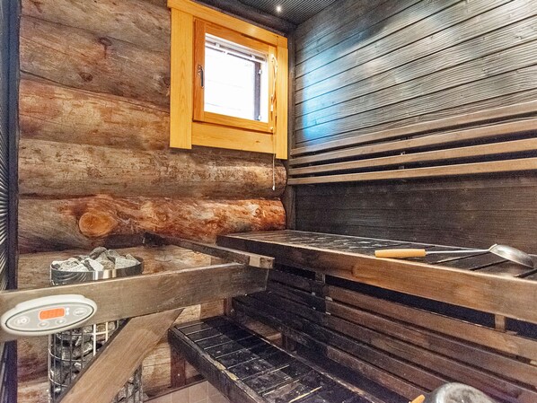 A log cabin interior with a wood stove, a window, and a metal sink.
