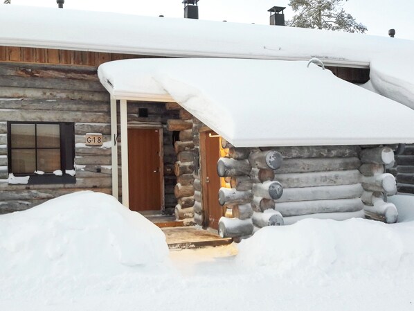 A log cabin with a wooden door and a number 'G18' on the wall.
