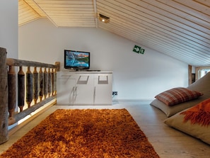 A room with a television on a white cabinet, a wooden railing, a brown rug, and a couch with pillows.