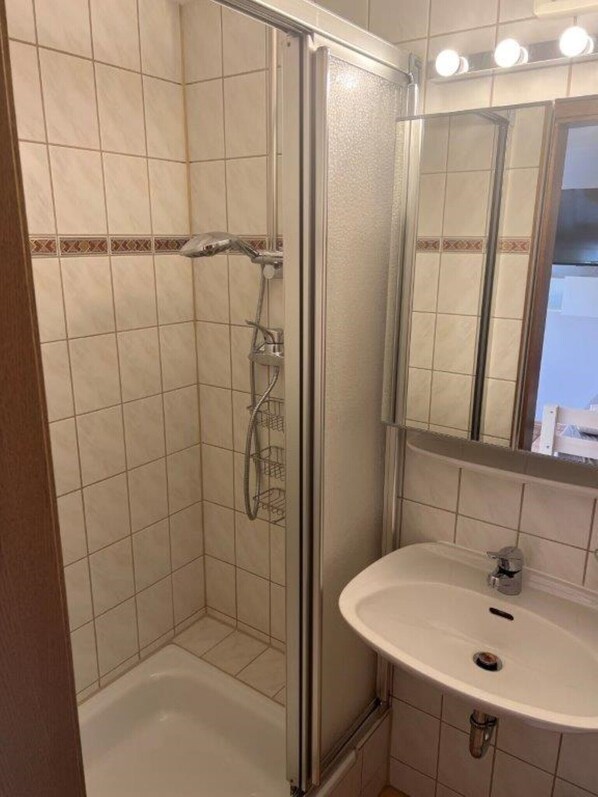 Ein Badezimmer mit einer gläsernen Duschkabine, einem weißen Waschbecken und einem Spiegel darüber.