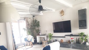 A modern living room with a flat-screen TV, blue sofas, a coffee table, and a large potted plant. - Villa Nyvioni, 3 ch, spa et Piscine (Agde)