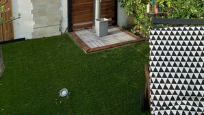A modern outdoor shower area with a vertical water feature, a wooden fence, and a well-maintained lawn. - Villa Nyvioni, 3 ch, spa et Piscine (Agde)