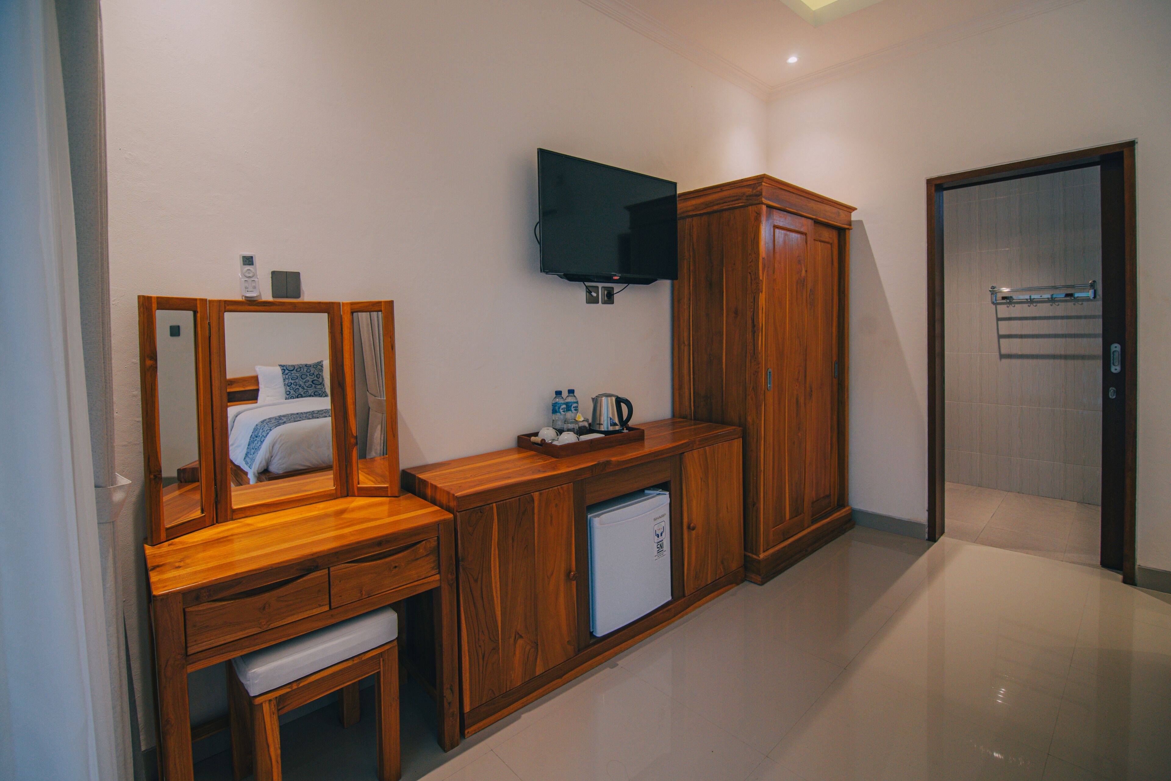 A hotel room with a wooden vanity, a small refrigerator, a flat-screen TV mounted on the wall, and a door leading to a bathroom.