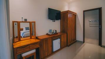 A hotel room with a wooden vanity, a small refrigerator, a flat-screen TV mounted on the wall, and a door leading to a bathroom.