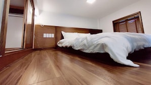 Ein Schlafzimmer mit Holzboden, einem Bett mit weißer Bettwäsche, einem Holz-Kopfteil und einem Fenster mit Jalousien.