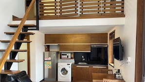 Eine moderne Wohnung mit einer Holztreppe, einer Küche mit Mikrowelle und Waschmaschine, einem schwarzen Ledersofa und einem Holzesstisch.