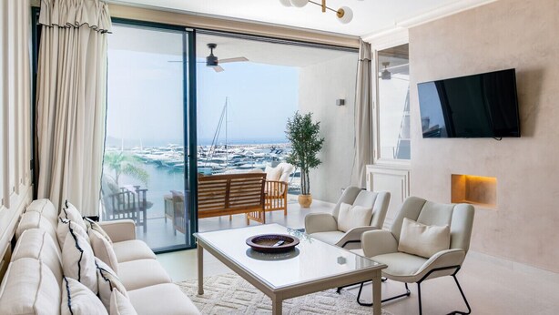 Ein modernes Wohnzimmer mit Glastür, die auf einen Balkon mit Blick auf eine Marina führt.