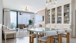 Ein modernes Wohnzimmer mit einem Glastisch, weißen Sofas und einer großen Schrankwand mit Regalen.