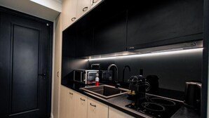 A modern kitchen with black cabinets, a black countertop, a built-in microwave, a coffee maker, and a gas stove. - Triple a - Chrisospiliotissis 7 (Athens)