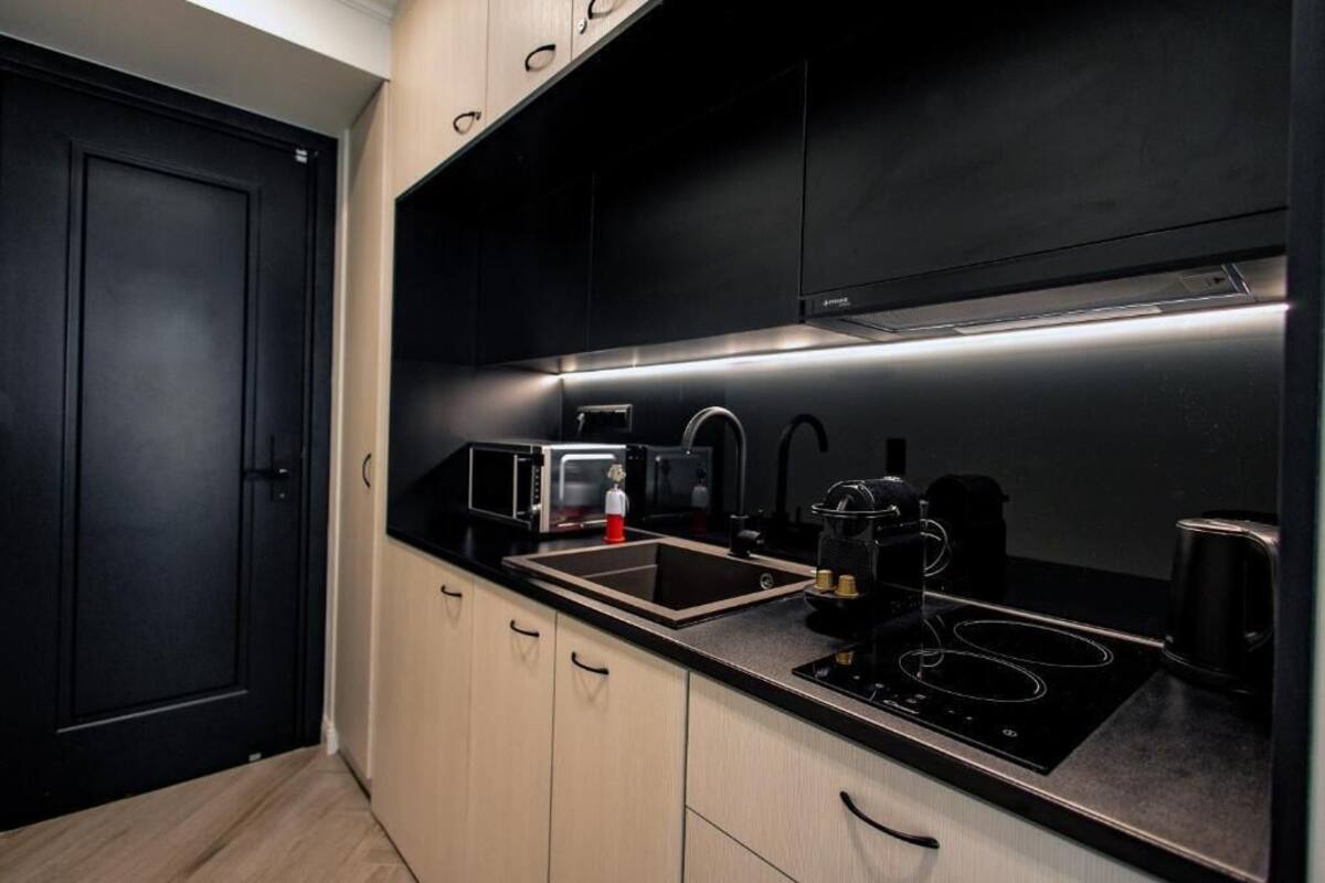 A modern kitchen with black cabinets, a black countertop, a built-in microwave, a coffee maker, and a gas stove.