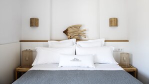 Un dormitorio con cama, almohadas blancas, un cabecero decorativo, mesitas de noche y una cesta tejida.