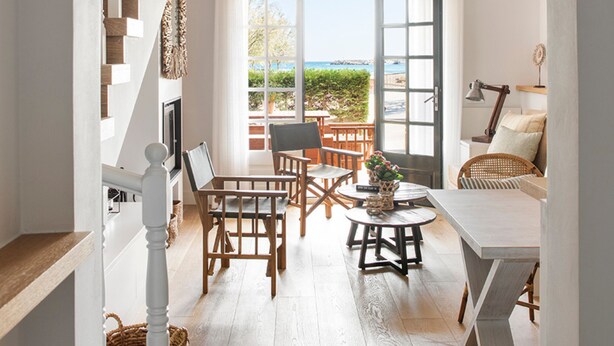 Una habitación luminosa con una escalera, un comedor con sillas y una mesa, y un ventanal con vistas al exterior.